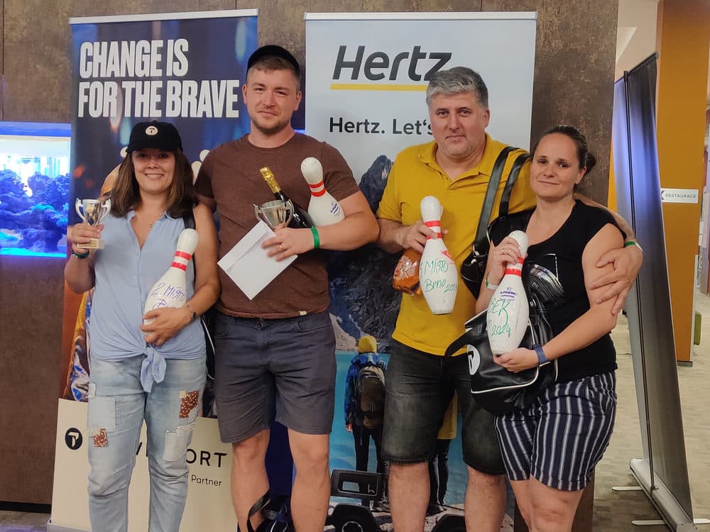 Vítězové brněnského bowlingu 2024 s poháry a kuželkami před bannery Hertz a Travelport
