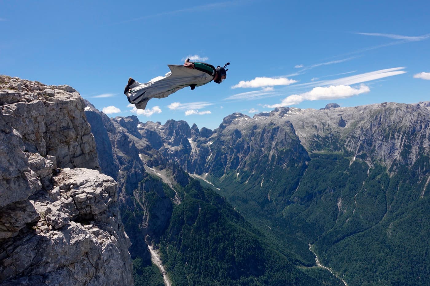 Wingsuitový letec se vrhá ze skalního útesu nad horským údolím