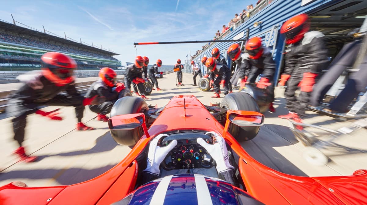 Tým mechaniků v červených přilbách čeká připravený na formuli vjíždějící do boxů