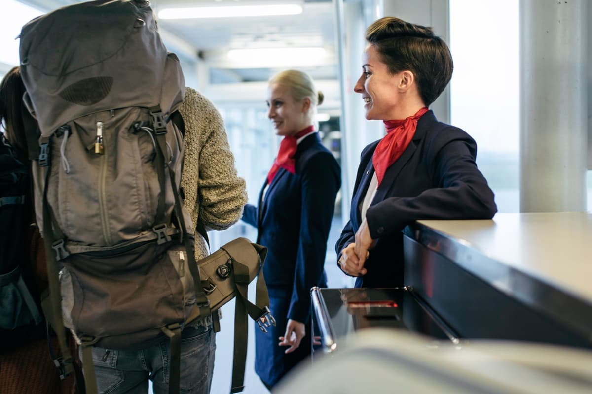 Usměvavé letušky vítají cestující s batohy u odbavovacího pultu