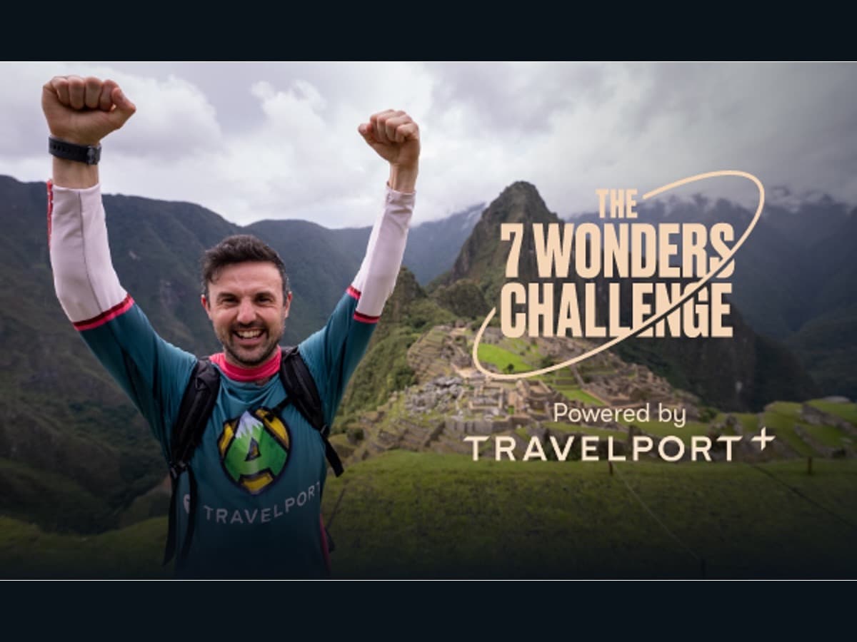 Jamie McDonald s rukama nad hlavou před Machu Picchu, v pozadí logo The 7 Wonders Challenge Powered by Travelport+